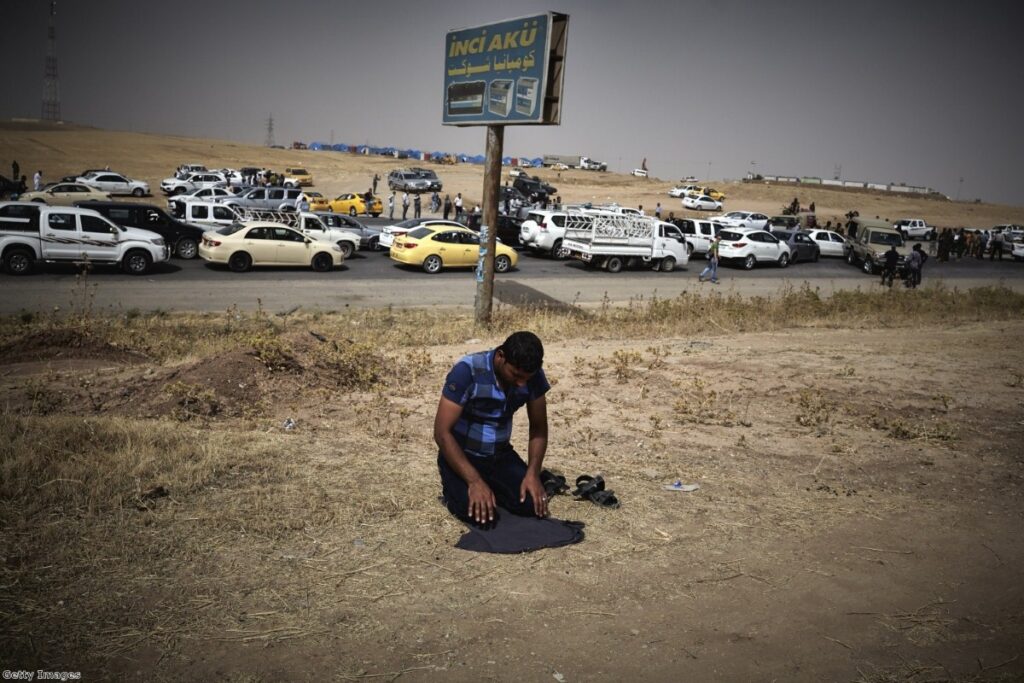 An Iraqi refugee fleeing from the city of Mosul prays at a checkpoint after Isis took the city last year