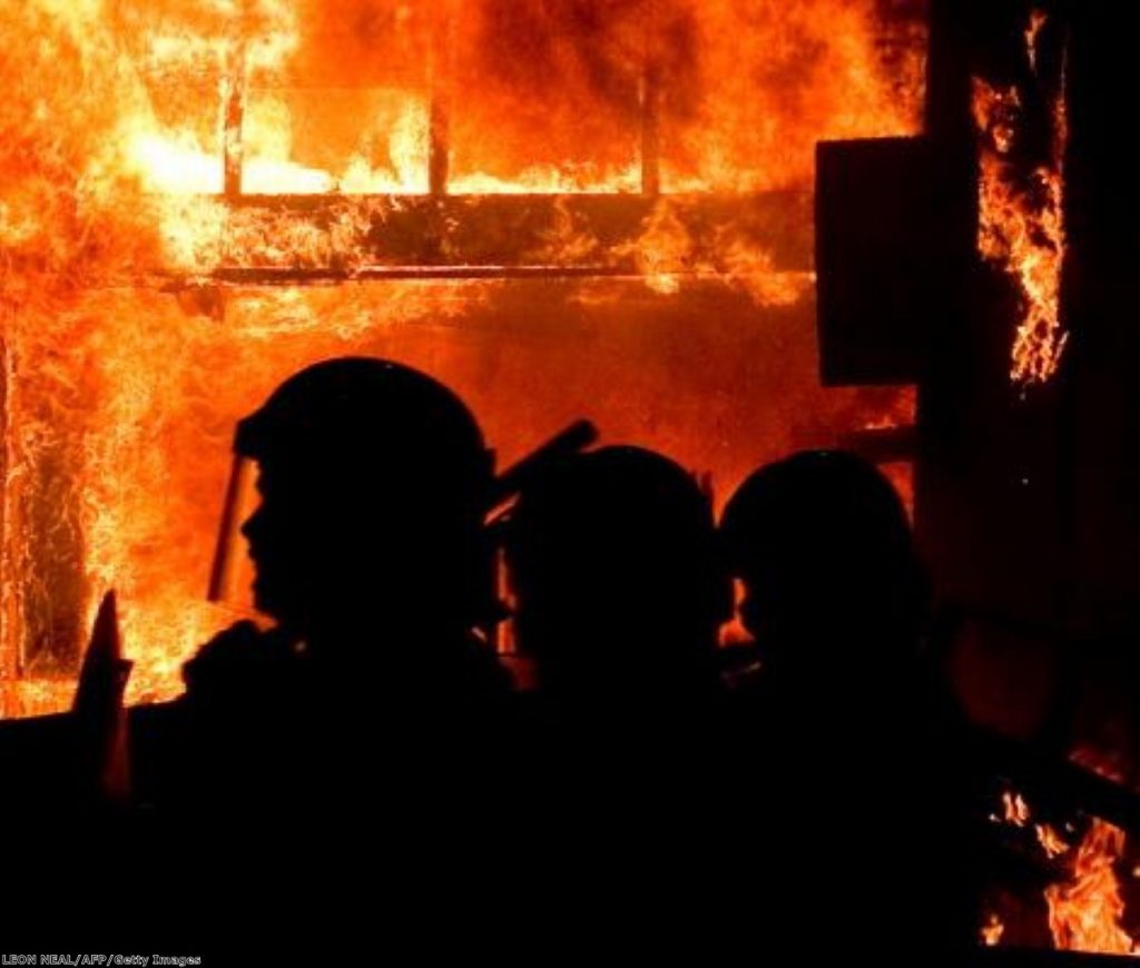 A shop burns in Tottenham, north London, as helpless riot police look on