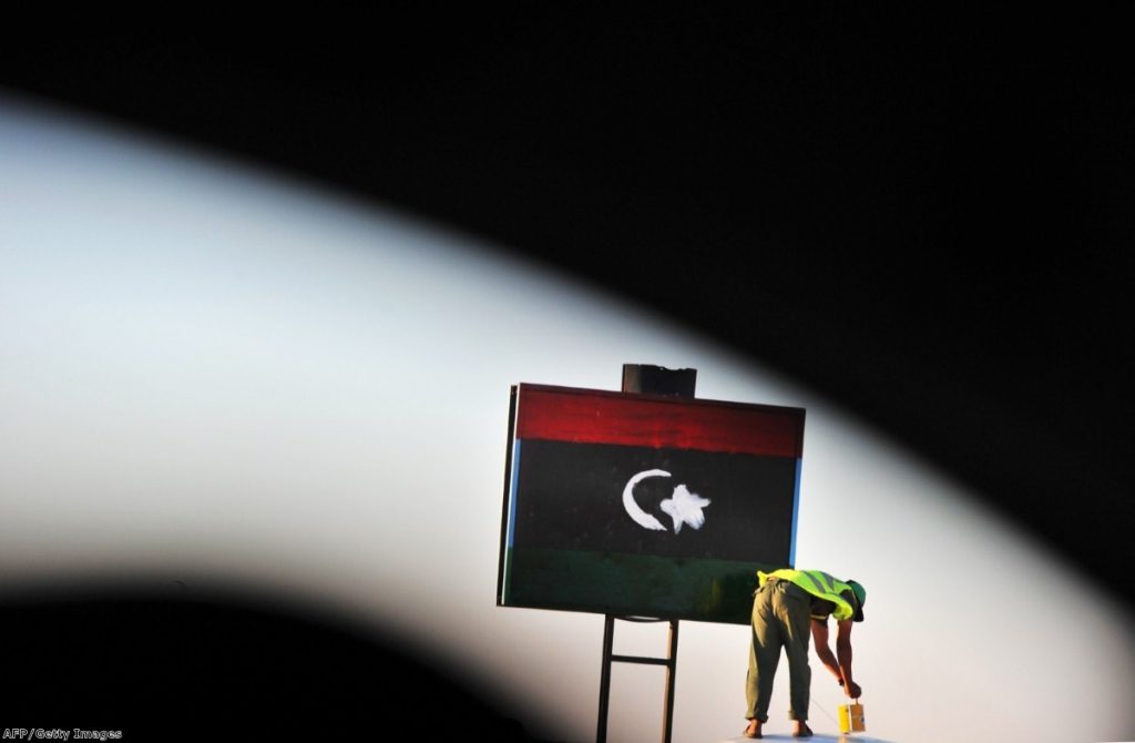 A checkpoint guard paints a Libyan flag on a sign at the checkpoint in Jadu yesterday.