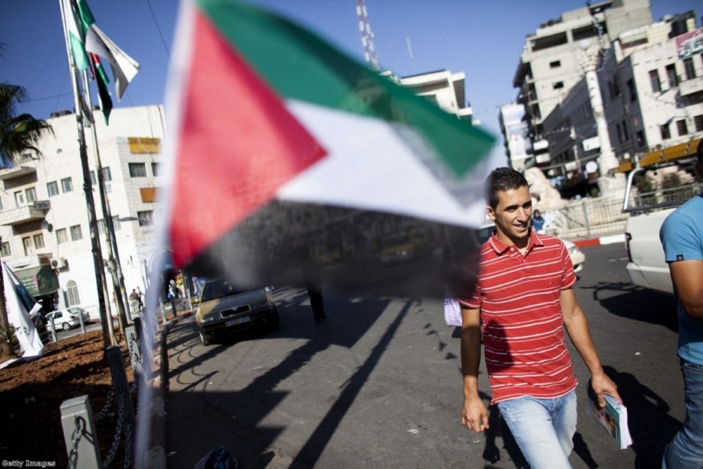 A Palestinian man walks past flags decorating a main round-about in Ramallah yesterday