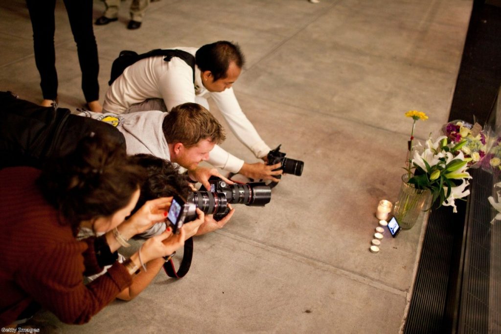 Photographers outside an Apple Store in New York strain to take of shot of candles, flowers, and an iPhone with Steve Jobs' photo displayed