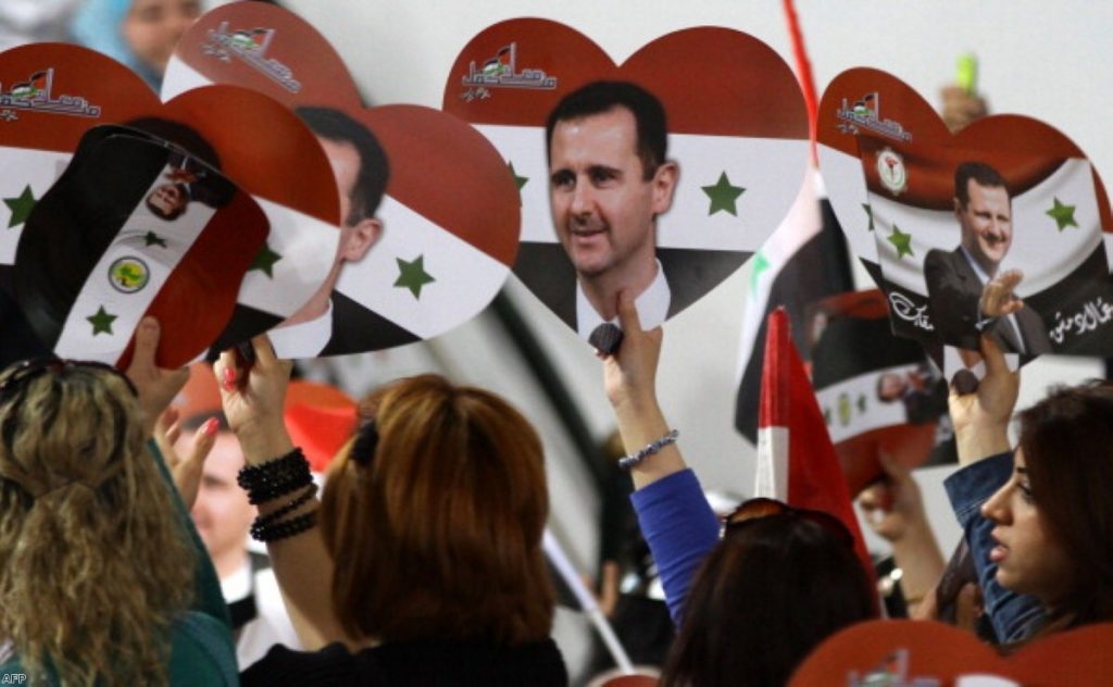 Assad supporters wave flags and placards during last year