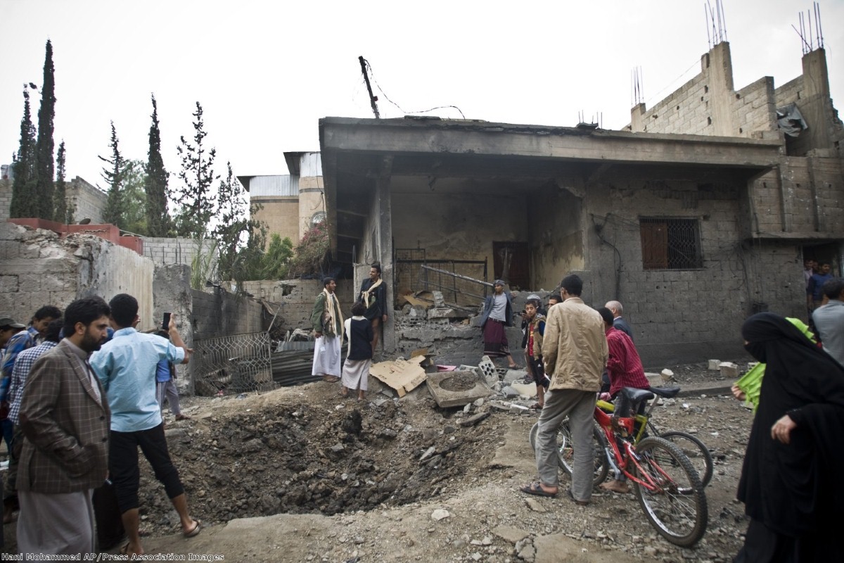 People stand by a crater and a house damaged by a Saudi-led airstrike in Sanaa, Yemen, Wednesday, May 27, 2015