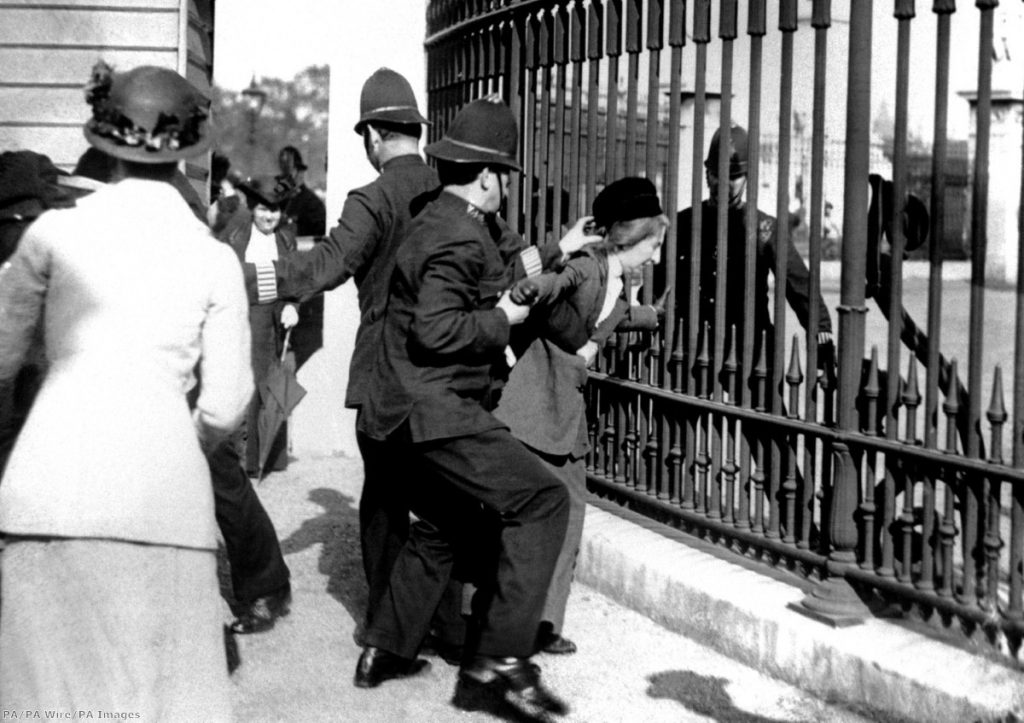 "A policeman restraining a demonstrator as suffragettes gathered outside Buckingham Palace"