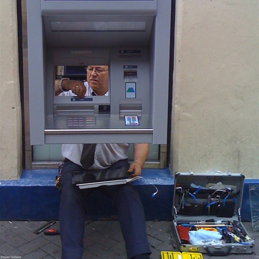 A man fixes a cash machine on a British street. Government sources admit the minimum wage could be cut, but analysts warn of effects on demand.