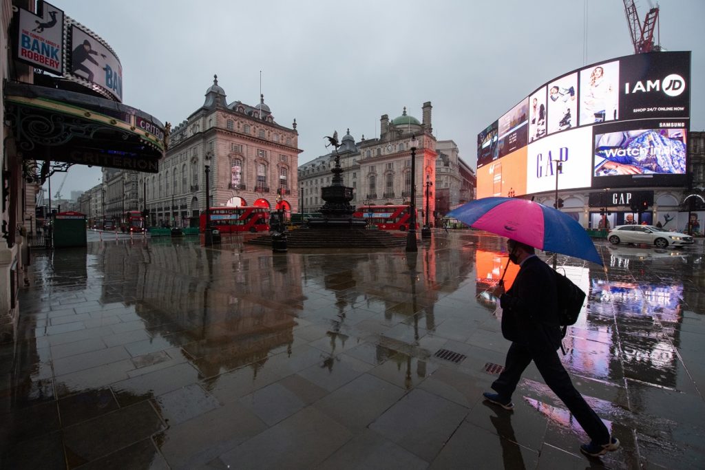 A man with an umbrella walks through a near empty Piccadilly Circus in London, during England's third national lockdown to curb the spread of coronavirus.