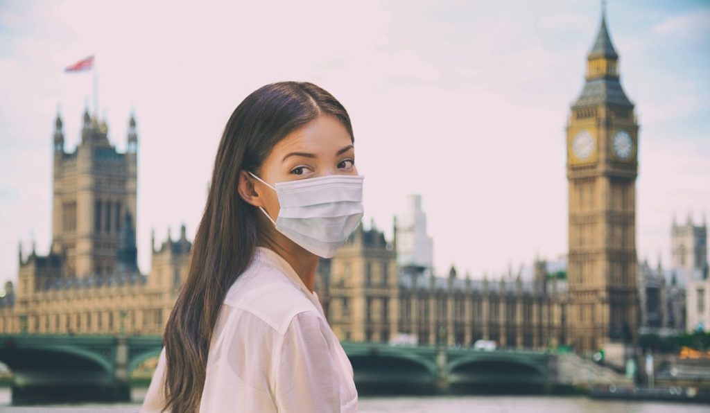 Corona virus travel corona virus spread prevention asian woman tourist wearing protective face mask on UK London city sightseeing holiday vacation. Famous british landmark background panoramic