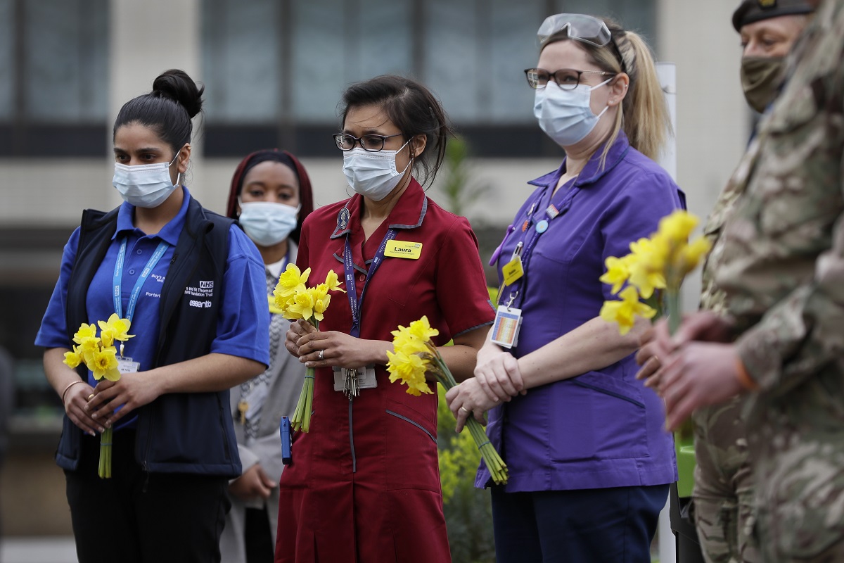 NHS staff lay flowers as they gather for a minute silence